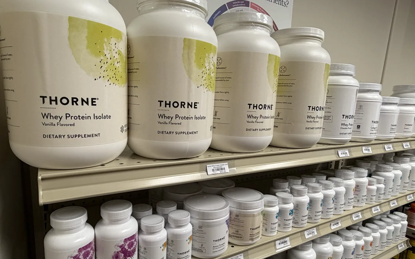 Tubs of Thorne Whey Protein Isolate on a shelf, above rows of Thorne supplement bottles.