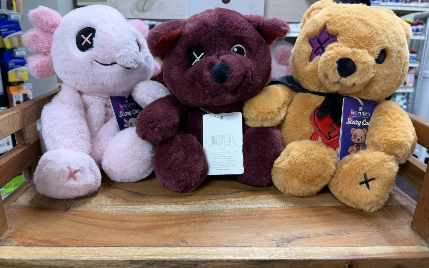 Three Warmies plush animals on a wooden shelf in the pharmacy.